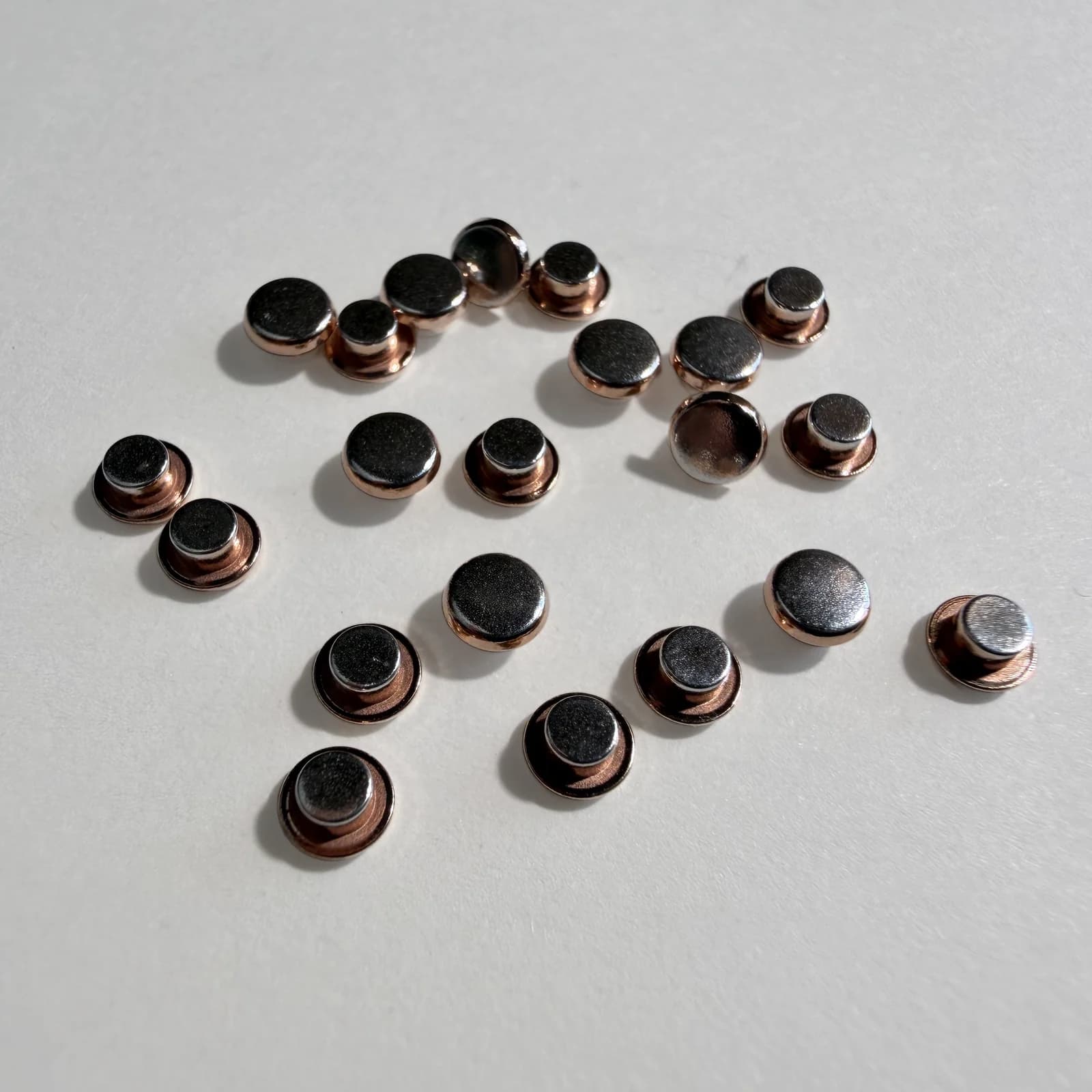 Custom trimetal electrical contact rivets arranged on a light neutral background.
