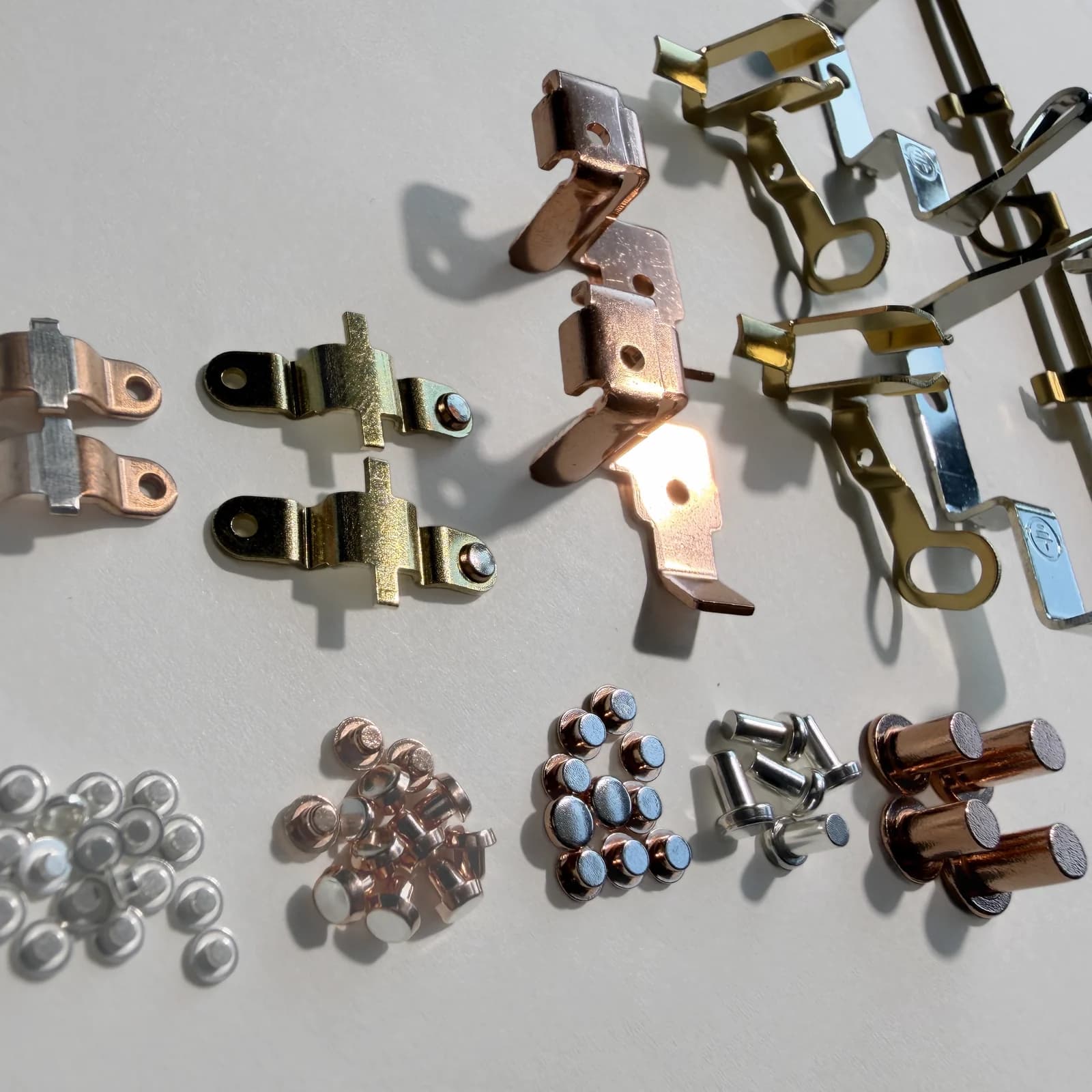 Photographed assortment of contact rivets, assemblies, and stamped conductive parts on a light work surface.
