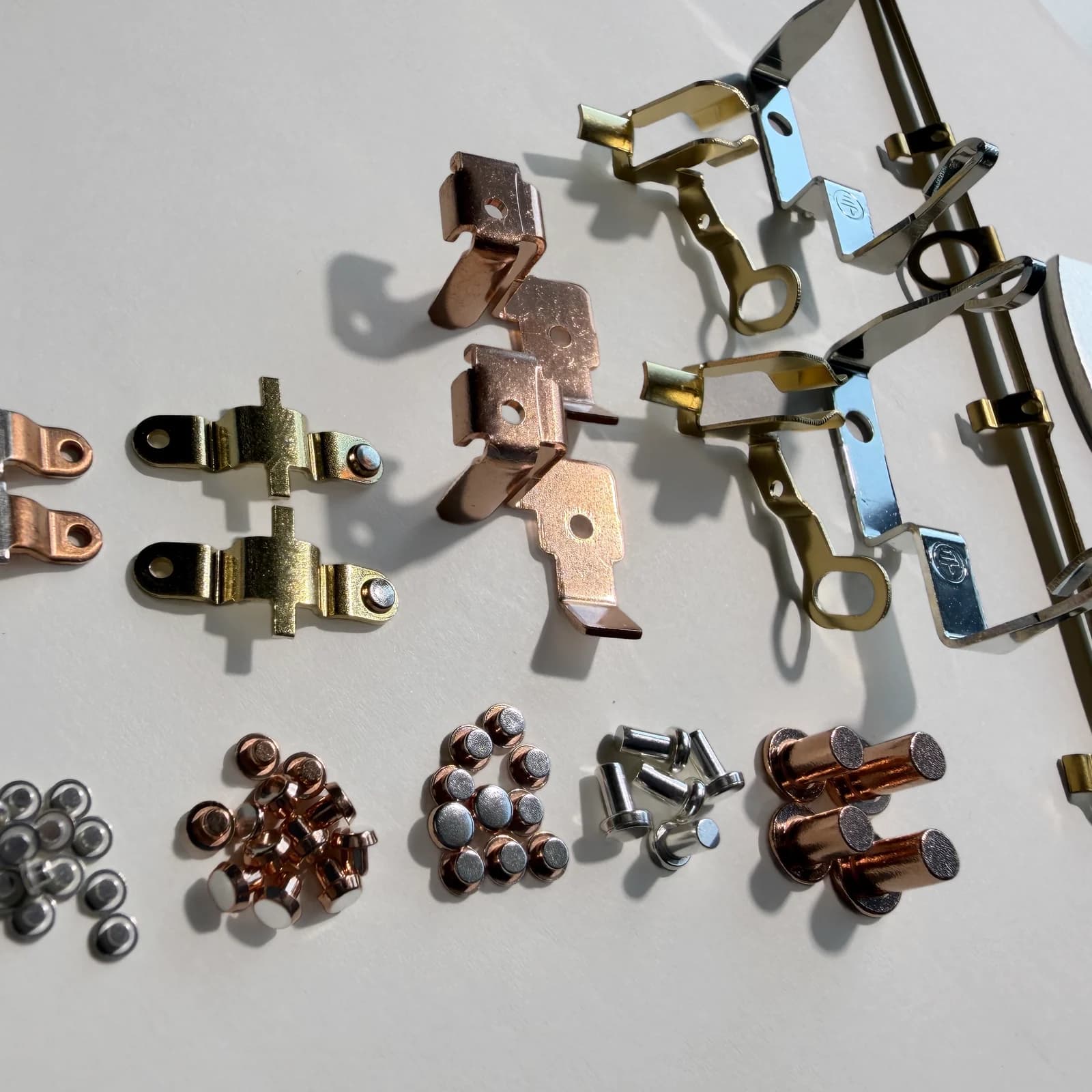 A photographed selection of custom electrical contact rivets and contact assemblies arranged on a light neutral work surface.